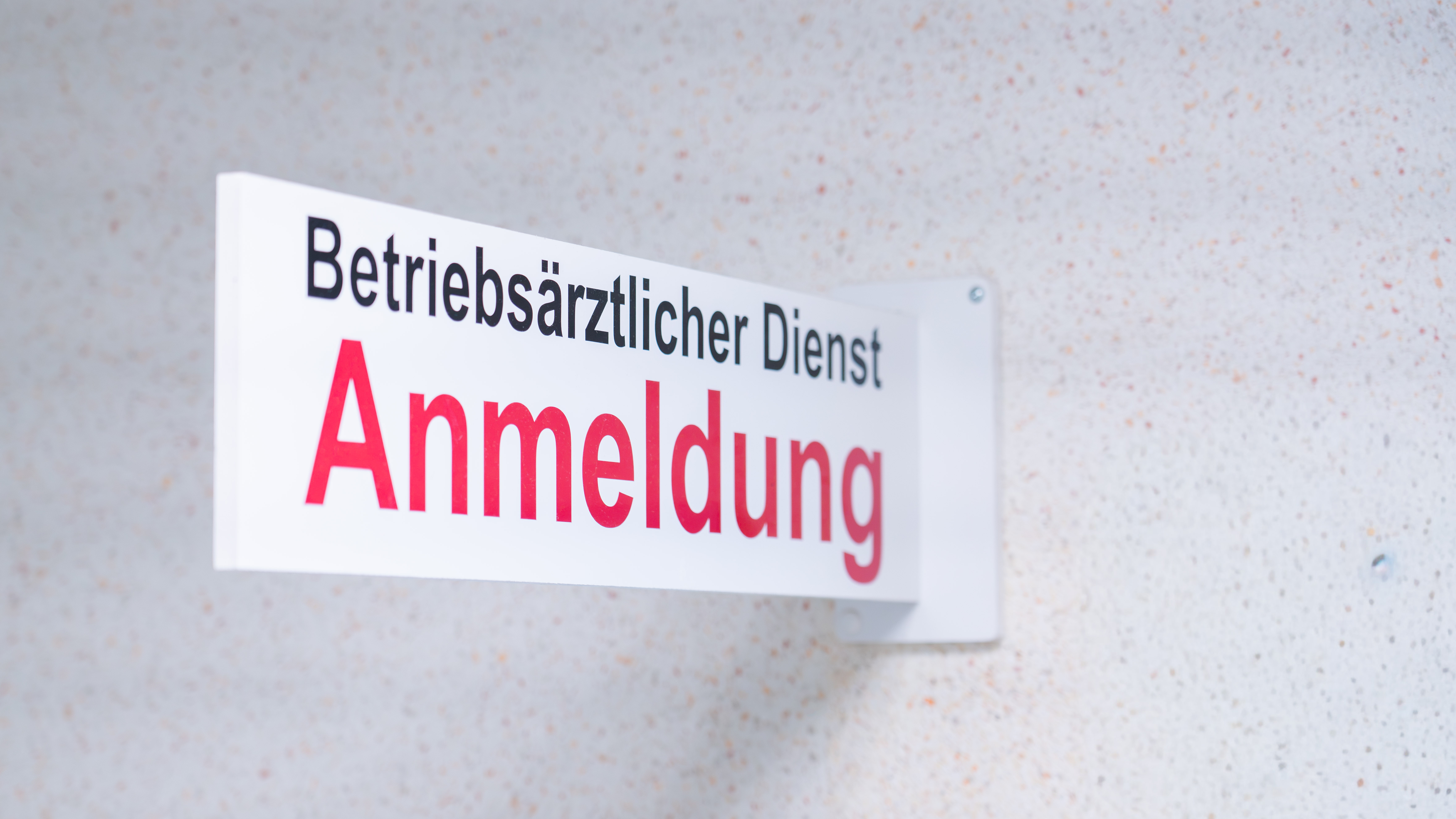 Schild mit der Aufschrift 'Betriebsärztlicher Dienst Anmeldung' an einer hellen Wand