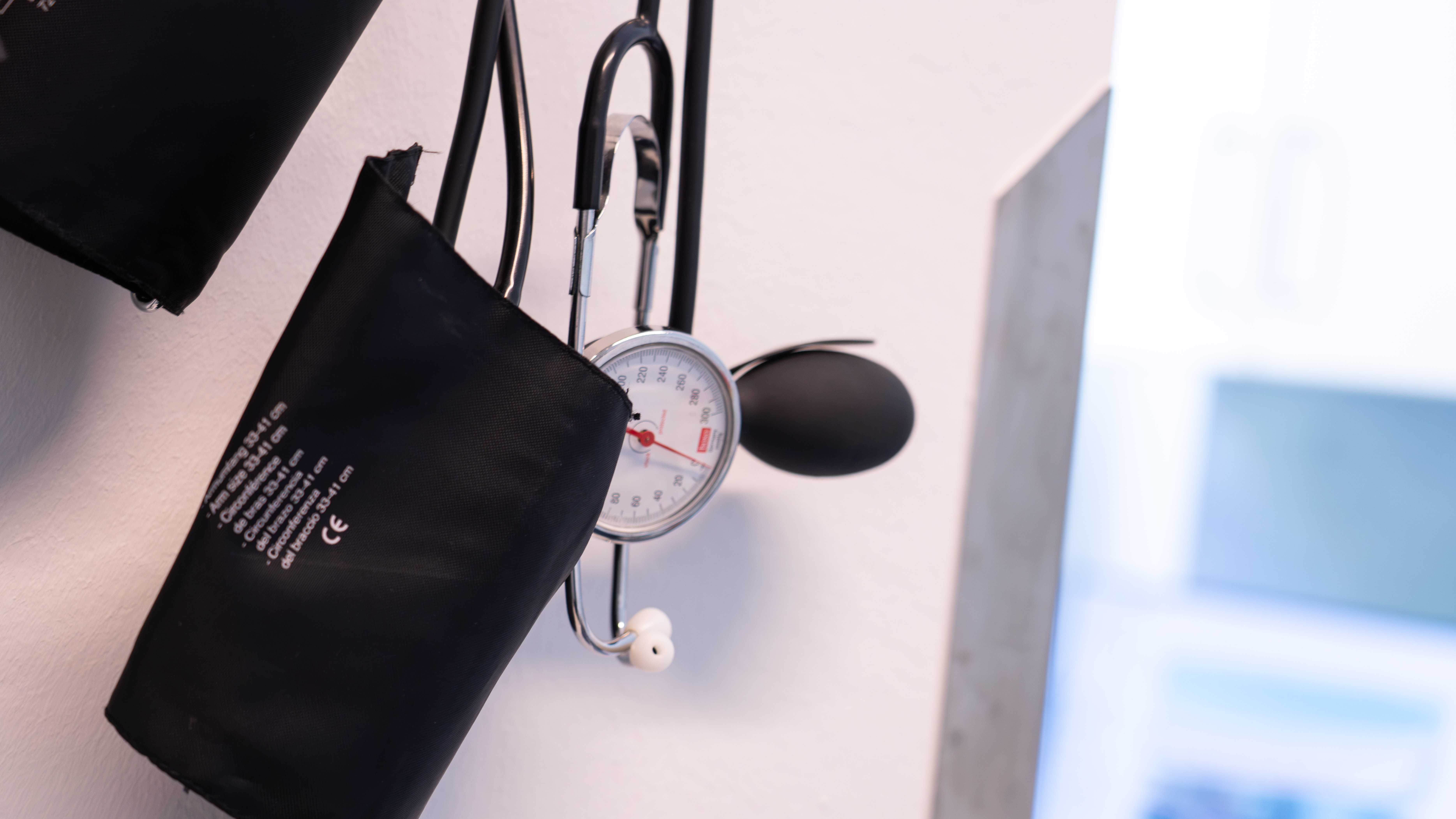 Blutdruckmanschette mit Manometer und Gummiball an einer Wandhalterung